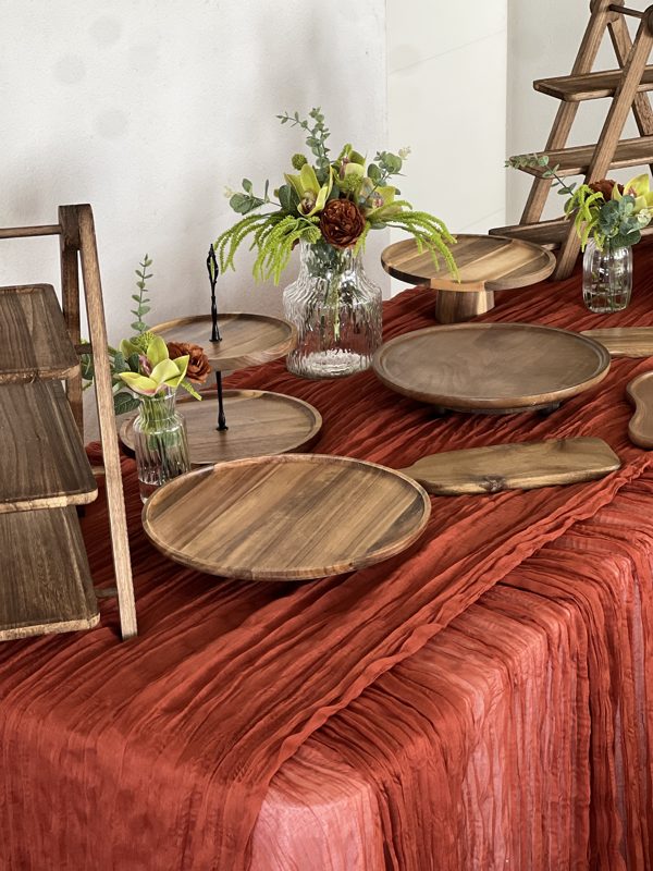 Présentoirs en bois naturel sur chemin de table terracotta : échelles, plateaux ronds et planches en acacia